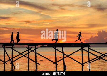 Silhouette Kind laufen mit glücklich auf dem hölzernen Steg während des Sonnenuntergangs auf Mantanani Island, Kota Belud, Sabah, Malaysia Stockfoto