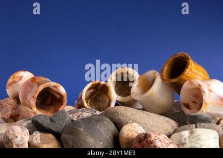 Stillleben mit sechs Onyx-Gläsern, die auf einem Haufen Kieselstein vor violettem Hintergrund liegen Stockfoto