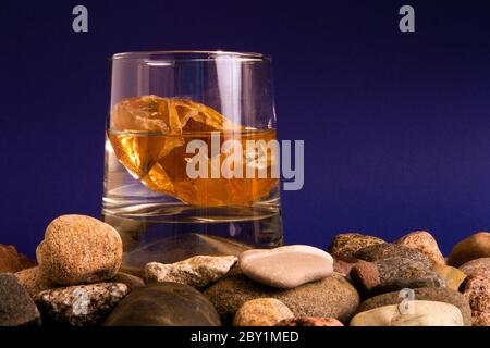 Glas mit Wasser und Bernstein im Inneren auf einem Haufen von Kieselsteinen stehen Stockfoto