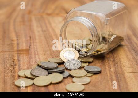 Münzen, die aus dem Glasgefäß verschüttet werden Stockfoto