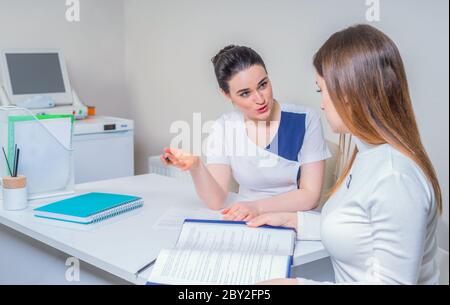 Junge Ärztin sitzt an ihrem Schreibtisch und plaudert mit der Patientin, während sie ihre Testergebnisse zeigt Stockfoto