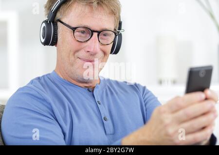 Glücklicher älterer Mann in der Brille, der Musik in Kopfhörern hört Stockfoto