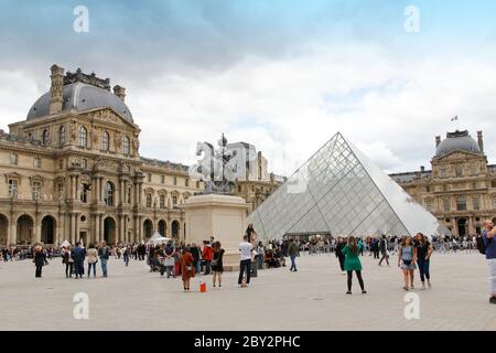 Paris, Frankreich - 18. Mai 2019: Touristen im Zentrum des Napoleon-Hofes mit der Louvre-Pyramide und Palast in bewölktem Tag Stockfoto