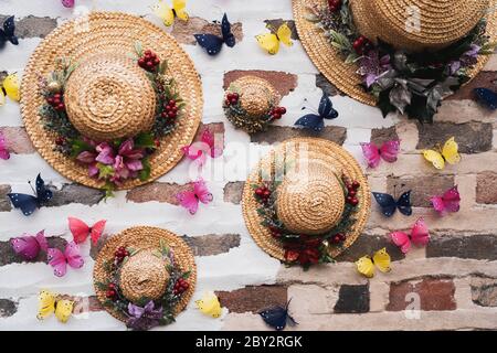 Fedora Sommer Sonnenhut und bunte getrocknete Blumen Anordnung und Schmetterlinge Dekoration hängen an einer Ziegelwand. Stockfoto