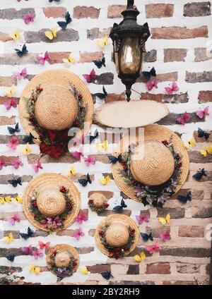 Leere hölzerne Schild an einer Vintage-Wandlampe hängen. Fedora Sommer Sonnenhut und bunte Schmetterlinge Dekoration auf einer Ziegelwand angezeigt. Stockfoto