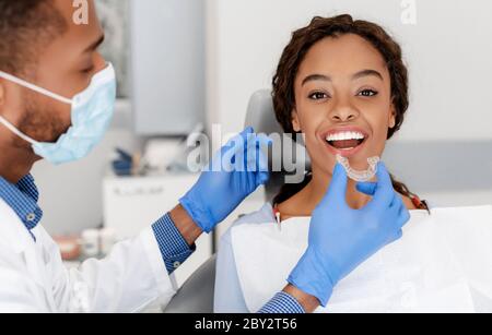 Zahnarzt, der unsichtbare Ausrichter auf die Zähne eines weiblichen Patienten anwendet Stockfoto