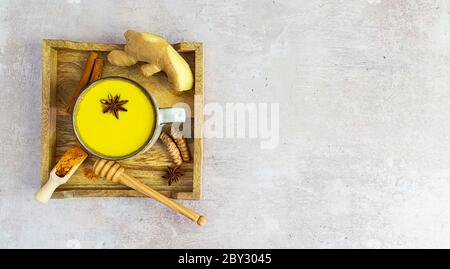 Holztablett mit goldener Kurkuma-Milch und Zutaten: Zimt, Honig und Ingwer mit Kopierraum Stockfoto