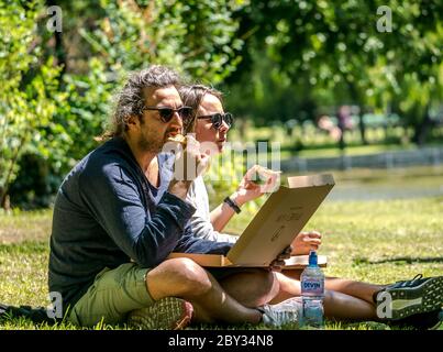 Bukarest/ Rumänien - 05.30.2020: Junges Paar beim Pizza essen. Die Leute im Cismigiu Park sitzen auf Gras und essen Pizze. Stockfoto