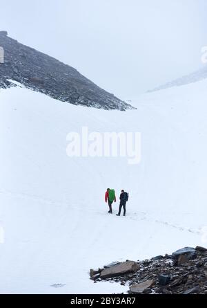 Rückansicht von männlichen Bergsteigern, die in gefrorenen schneebedeckten Bergen wandern. Wanderer mit Rucksäcken, die durch den Schnee wandern und auf den Gipfel gehen. Konzept des Reisens, Alpinismus und Bergsteigens. Stockfoto