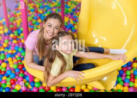 Fröhliches Mädchen mit ihrer Mutter auf Rutsche bei Indoor-Kinderspielplatz sitzen Stockfoto