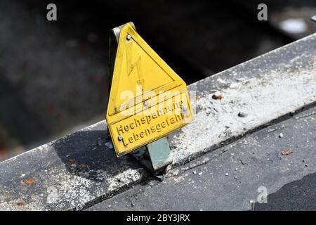 Warnschild, HOCHSPANNUNGS-LEBENSGEFAHR! Mit Blitzsymbol auf einer Brücke über eine Freileitung einer Eisenbahnlinie. Weltweit verwendet Stockfoto