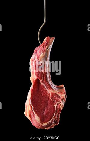 Rind Ribeye Steak Knochen-in auf Stahlhaken auf schwarzem Hintergrund Stockfoto