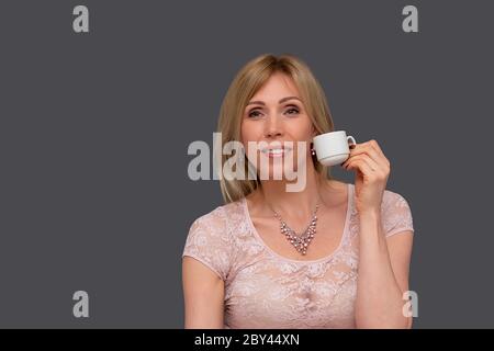 Schöne Frau mit Tasse Tee oder Kaffee. Studio-Porträt einer verträumten blonden Frau, die eine Tasse in den Händen hält, trinkt frisches leckeres Getränk Stockfoto