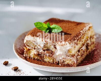 Perfekte hausgemachte Tiramisu Kuchen mit frischer Minze. Tiramisu Teil auf rosa Platte über weißem Marmor Hintergrund. Köstliche No Bake Tiramisu bei natürlichem Tageslicht. Nahaufnahme Stockfoto