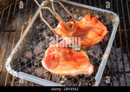 Nahaufnahme von frisch zubereiteten Burgern und Koteletts, die im Frühsommer auf einem kleinen Grill in einem großen Garten gesehen werden. Stockfoto