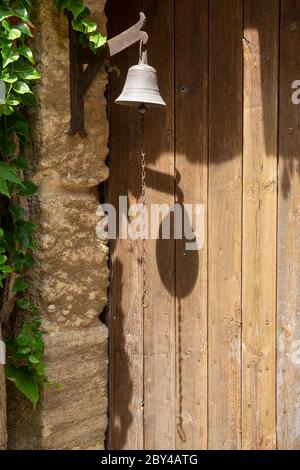 Eine antike Türglocke in einem Dorf in der Provence, Frankreich, wirft einen Schatten auf eine verwitterte Holztür Stockfoto