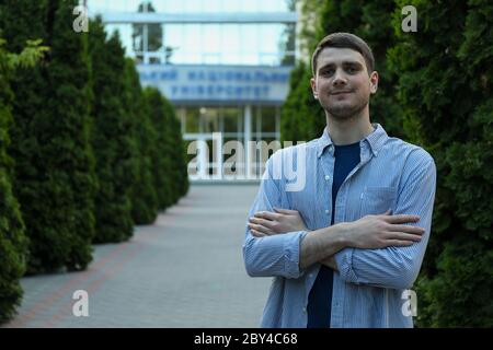 Junger Mann im Hemd mit gefalteten Händen gegen die Universität. Studie Stockfoto