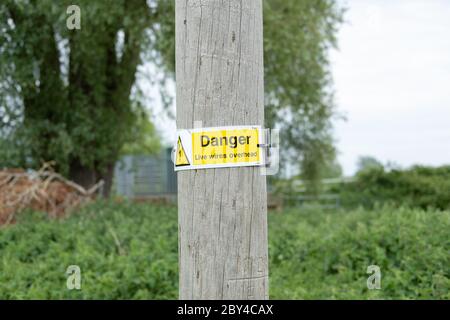 Neu installiertes Warnschild an einem Holzmast, an dem Hochspannungsnetzkabel installiert sind. Wird verwendet, um einen Teil eines regionalen Wohngebiets zu versorgen Stockfoto