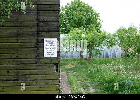 Warnschild an einer hölzernen Scheune Außenwand angebracht, Warnung Hundebesitzer und Wanderer oben den Weg zu halten Stockfoto