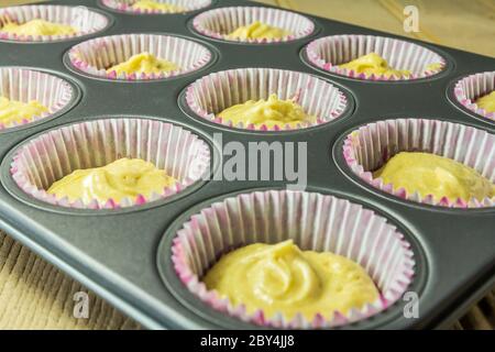 Tasse Kuchen Mischung in Papierhüllen in einer Pfanne bereit, in einem Ofen gebacken werden Stockfoto