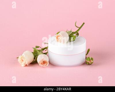 Gesichtscreme und kleine Rosen in hellem Pfirsich-Farbe auf einem pastellrosa Hintergrund. Kosmetik für feuchtigkeitsspendende und reinigende. Haut-, Haar- oder Körperpflege. Stockfoto