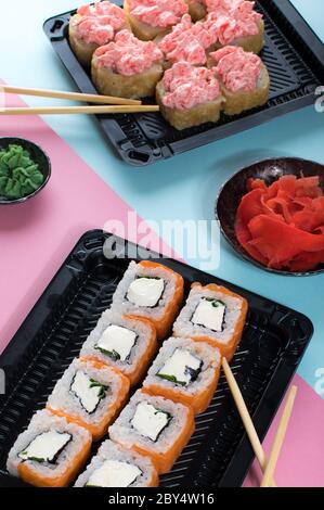 Sushi-Brötchen mit roter Mayonnaise-Sauce und Philadelphia in schwarzer Schachtel. Lieferung von Lebensmitteln. Rosa und blauer Hintergrund Stockfoto