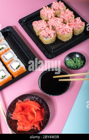 Sushi-Brötchen mit roter Mayonnaise-Sauce und Philadelphia in schwarzer Schachtel. Lieferung von Lebensmitteln. Rosa und blauer Hintergrund Stockfoto