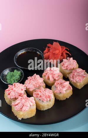 Sushi-Brötchen mit roter Mayonnaise-Sauce auf schwarzem Teller serviert. Nahaufnahme des Fotos Stockfoto