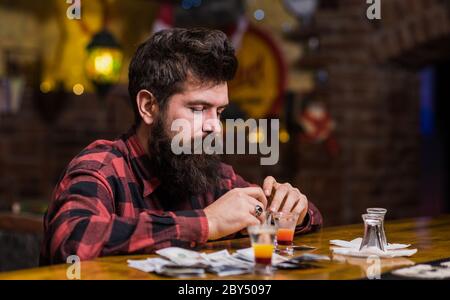 Depressiv und traurig Mann sitzen allein in der Bar oder Pub in der Nähe der Bar-Theke. Depression und Alkoholismus Konzept. Guy verbringen Freizeit in der Bar, defokussed Hintergrund. Hipster auf nachdenklichen Gesicht hält Bargeld in den Händen. Stockfoto