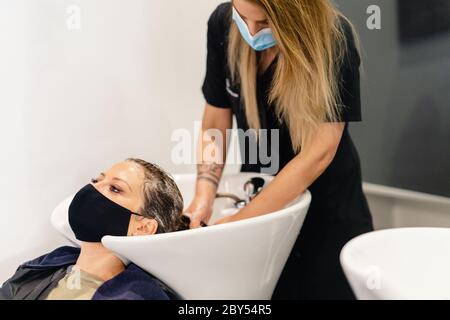 Friseursalon, der den Kopf eines Kunden in einem Salon wäscht, geschützt durch eine Maske gegen Covid-19 Stockfoto