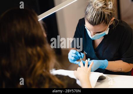 Nahaufnahme der Kosmetikerin, die in einem Beauty Center die Nägel ihrer Klientin in blauen und gelben Nagellack malt Stockfoto