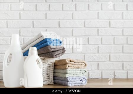Waschküche. Flaschen mit Waschmittel Gel und üppigen Handtücher in Korb auf Holztisch mit weißen Ziegelwand auf Hintergrund. Stockfoto