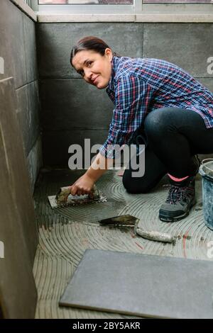 Maurerin legt einen neuen Fliesenboden Stockfoto