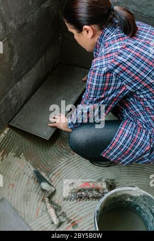 Baumeisterin legt einen neuen Fliesenboden Stockfoto