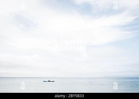 Ein Mann, der an einem ruhigen, aber bewölkten Tag einen blauen Kajak im Ozean am Walzerville North Beach in Victoria Australia benutzt Stockfoto