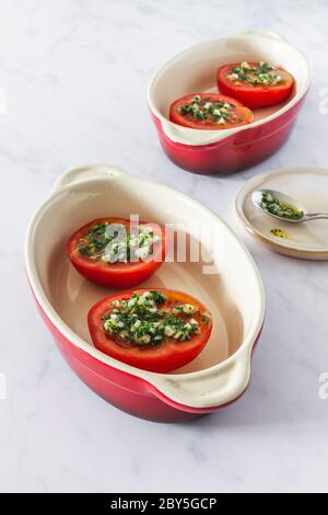 Halbe Tomaten mit Olivenöl, Knoblauch und Petersilie in kleinen roten Gerichten Stockfoto