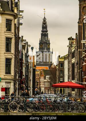 Viele Fahrräder parkten in der Straße von Amsterdam. Kirchturm auf einem Hintergrund, Niederlande. Stockfoto