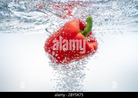 Fallende rote Paprika in ökologischem klarem Wasser. Nahaufnahme. Stockfoto