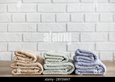 Drei gefaltete Badetücher auf Holztisch und weiße Ziegelwand auf Hintergrund. Beige-, Lavendel- und Minzfarben Stockfoto