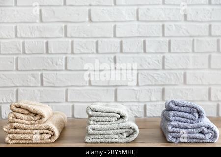 Drei gefaltete Badetücher auf Holztisch und weiße Ziegelwand auf Hintergrund. Beige-, Lavendel- und Minzfarben Stockfoto