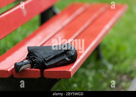 Vergessen schwarz gefaltet Regenschirm auf hölzernen Parkbank liegend bei starkem Regen Stockfoto