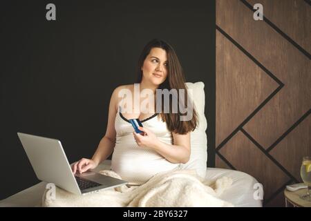 Das Porträt einer wunderschönen Frau tun Online Shopping mit Laptop sitzend auf dem Bett Stockfoto