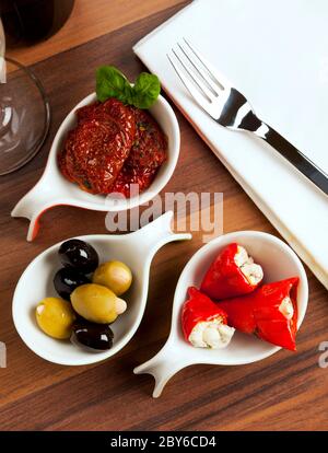 Vielfalt von Antipasti auf Verkostungslöffel: Marinierte getrocknete Tomaten, schwarze und grüne Oliven, gefüllte rote Paprika, Blick aus dem hohen Winkel Stockfoto