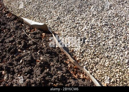 Metalleinkantung, die Schmutz und verschiedene Schotterfarben in einem Park voneinander trennt Stockfoto