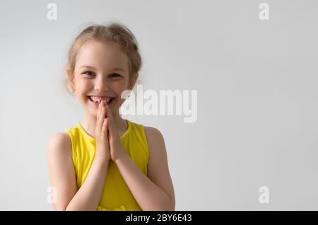 Hübsches kleines Mädchen ist glücklich und froh, etwas zu bekommen, von dem sie träumte, lächelnd und die Hände zusammenfaltet. Kindheit, süß und positiv, happi Stockfoto