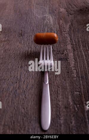 Wurst mit Rauch. Heiße gekochte Wurst auf einer Gabel mit dem Effekt von Dampf auf Vintage-Holztisch. Stockfoto