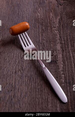 Wurst mit Rauch. Heiße gekochte Wurst auf einer Gabel mit dem Effekt von Dampf auf Vintage-Holztisch. Stockfoto