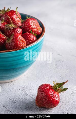 Frische reife Erdbeerfrüchte in blauer Schale, Sommer-Vitaminbeeren auf grauem Steingrund, Winkelansicht Stockfoto