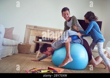 Glückliche Familie spielt auf Fitness-Ball im Wohnzimmer Stockfoto