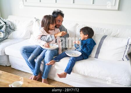 Vater und Kinder essen Popcorn auf dem Sofa im Wohnzimmer